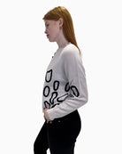 Side profile of model in the Faber Woman cream abstract print jumper and black trousers