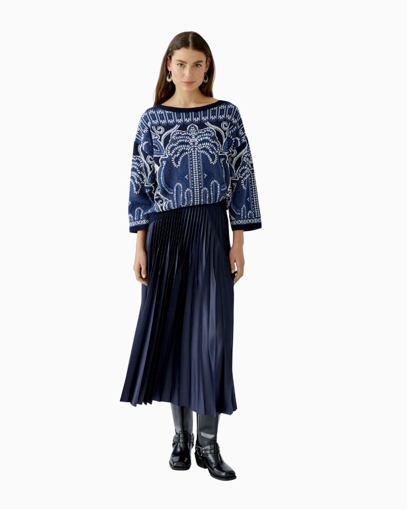 Model walking in dark blue Oui pleated skirt, mid-swing