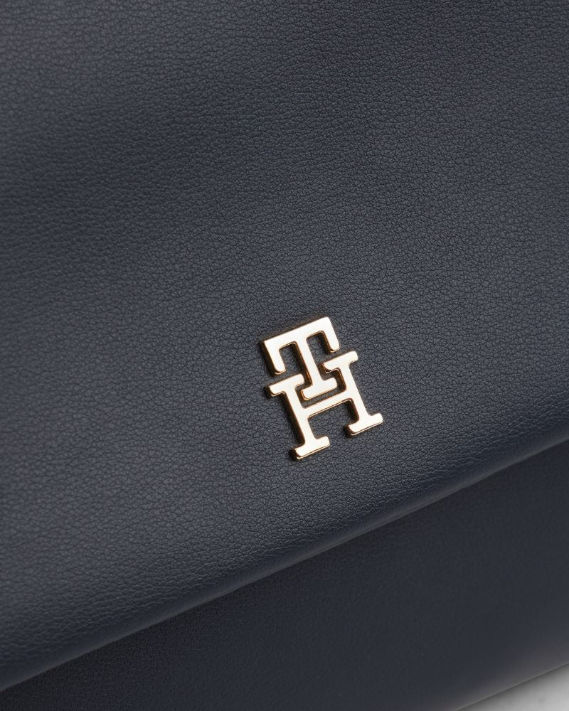 Close up of Tommy Hilfiger navy shoulder bag with monogram plaque and removable crossbody strap