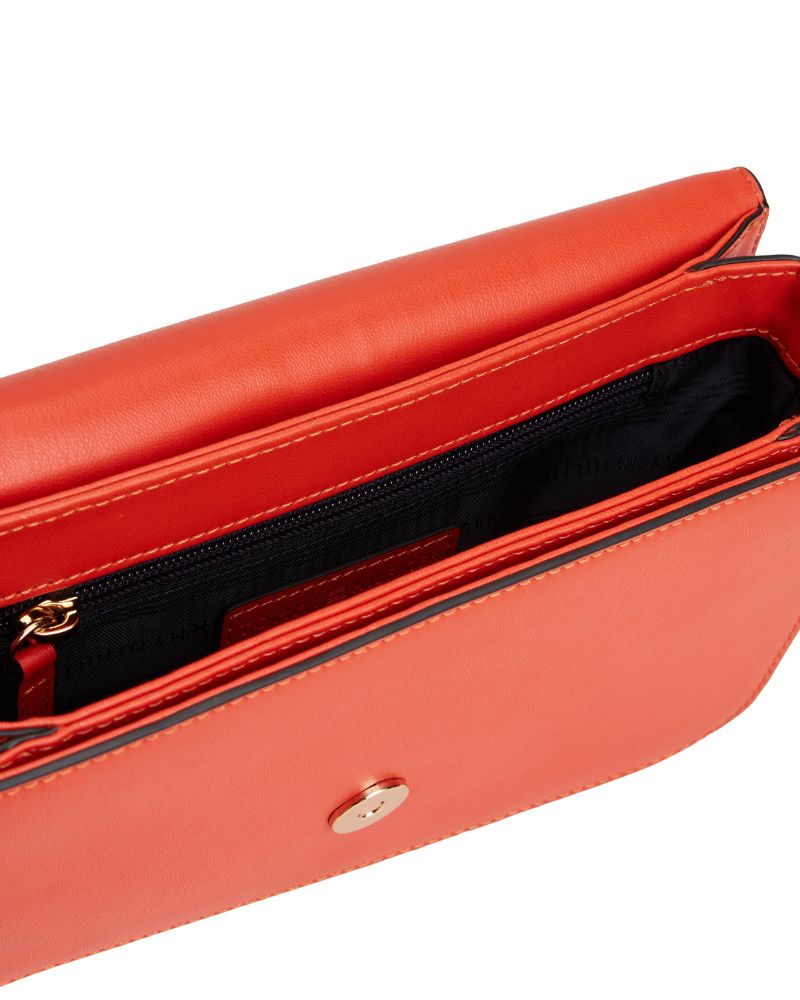 CLose up of Tommy Hilfiger orange crossover bag with flap closure and adjustable strap