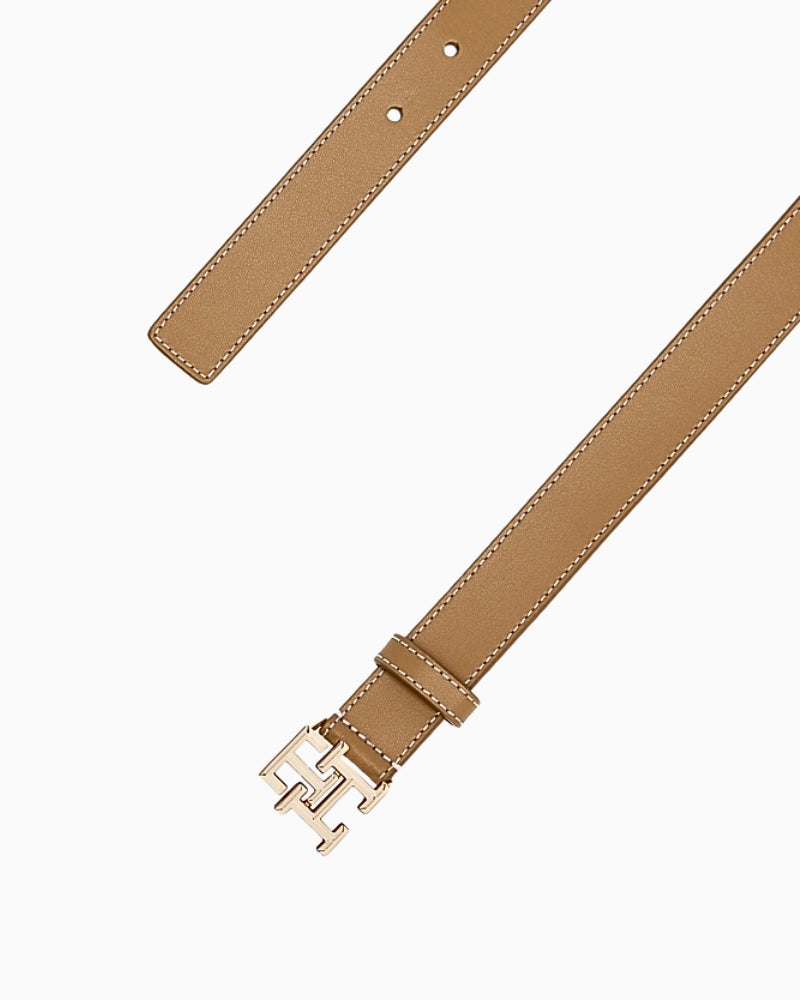 Close-up of tan Tommy Hilfiger belt showing adjustable strap and signature gold ‘TH’ buckle
