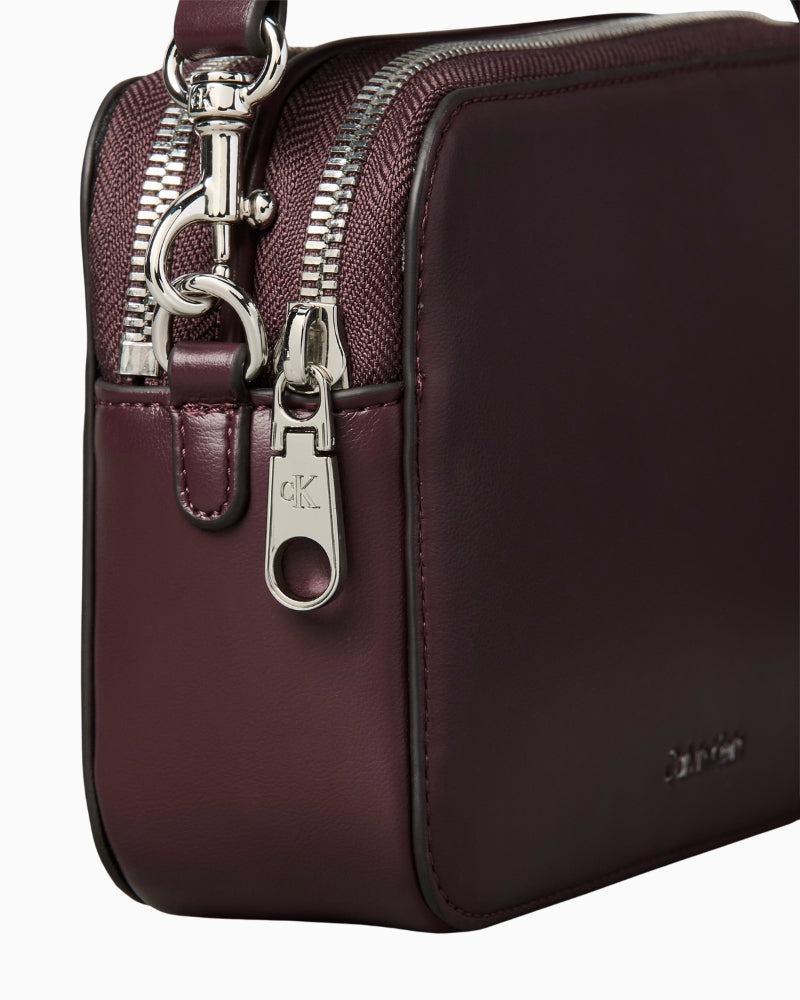 Side profile of the Calvin Klein brown camera bag in polyurethane with double webbing straps.