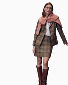 Woman styling pink cable knit jumper over a tweed blazer and skirt with tall brown boots