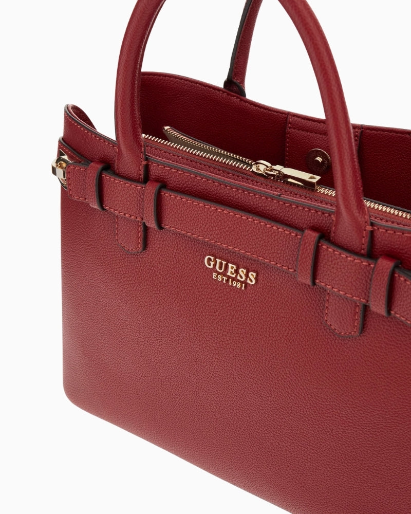 Close‑up of red faux leather texture and charm at handle base on Guess Gregoria bag