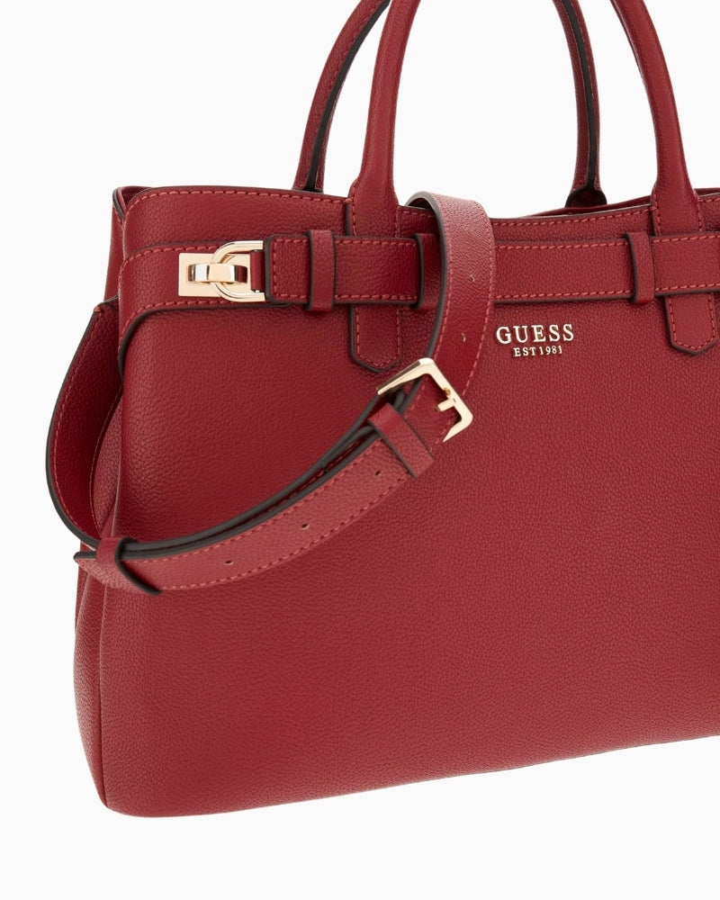 Close‑up of red faux leather texture and charm at handle base on Guess Gregoria bag