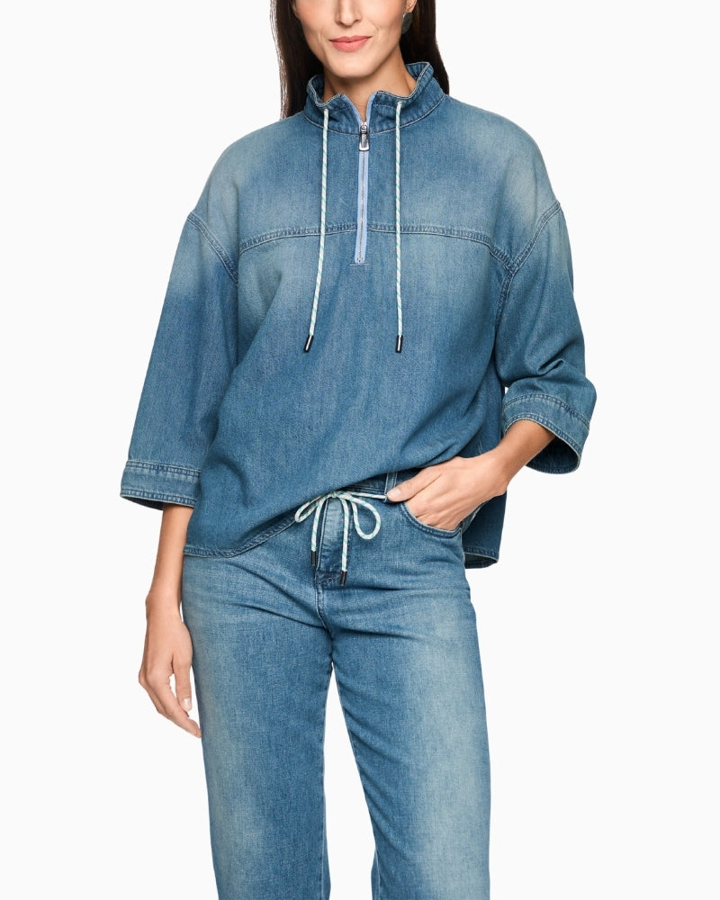 Woman wearing Marc Cain blue denim-style blouse front view with zip neckline – Áines Boutique