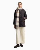 Model wearing cream tartan scarf draped over dark outerwear outfit