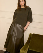 Model wearing Oui khakimidi skirt styled with knit jumper and ankle boots