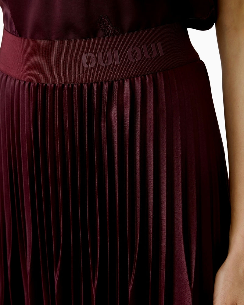 Close-up of OUI logo elastic waistband on glossy bramble berry pleated skirt