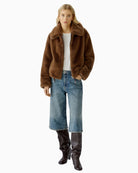 Model wearing taupe faux fur jacket styled with cropped jeans and boots