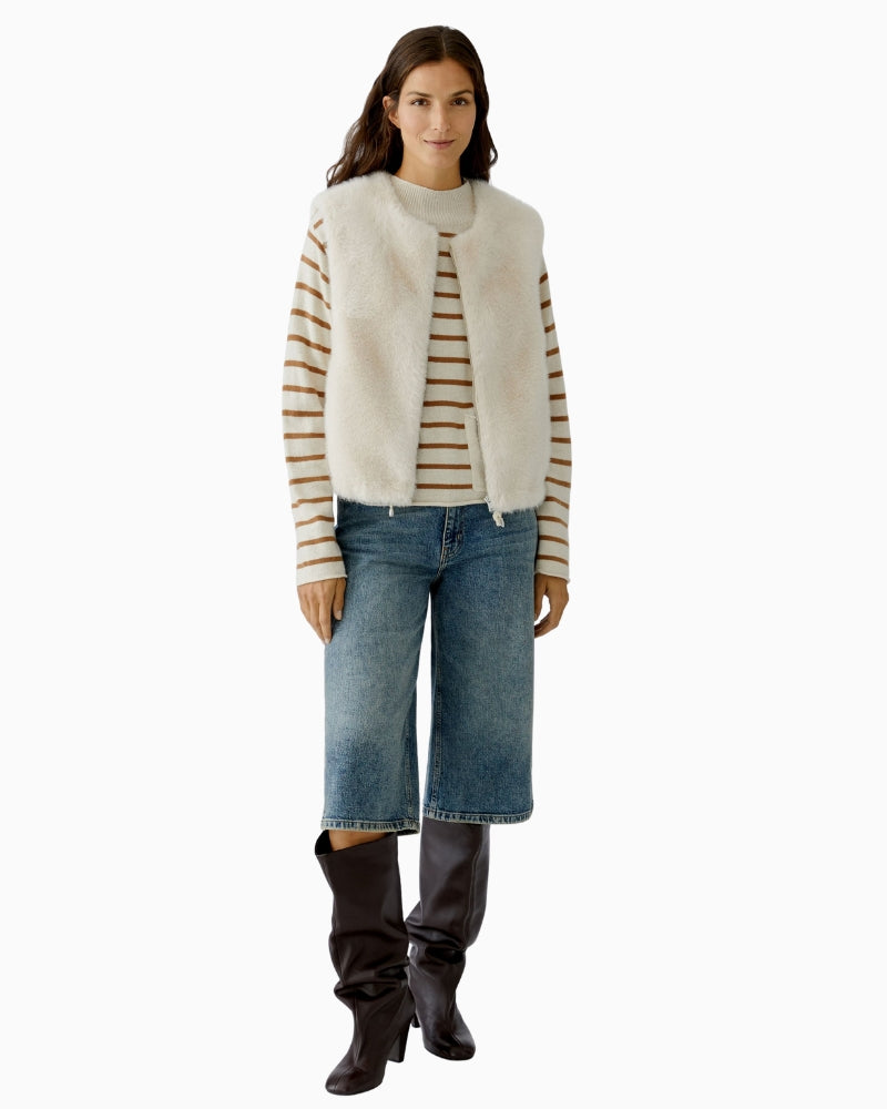 Model wearing off white faux fur waistcoat layered over knit and cropped jeans