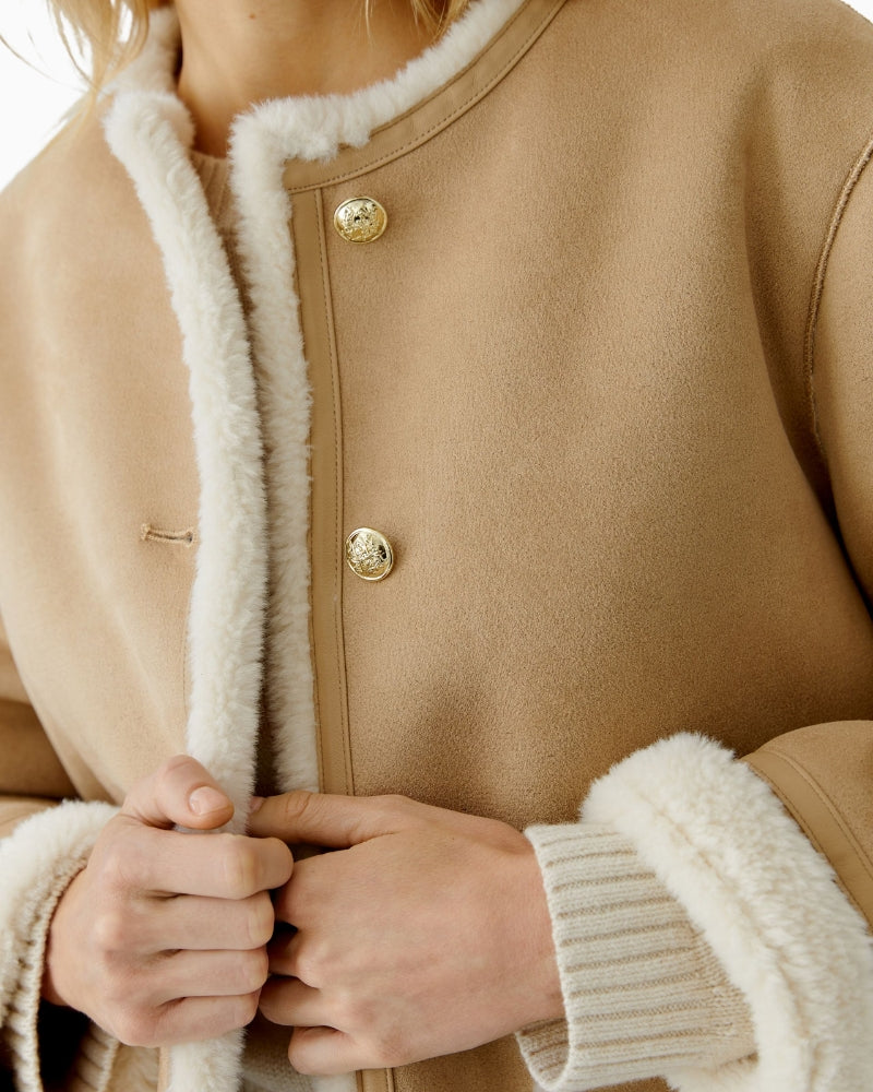 Close-up of gold crest button detail on camel faux leather jacket by Oui