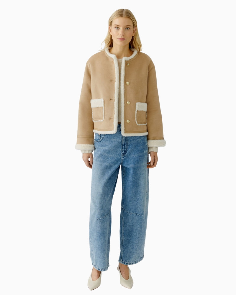Model wearing camel faux leather jacket layered over knit and jeans