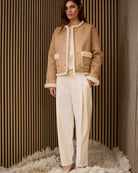 Model wearing camel faux leather jacket layered over knit and off white trousers