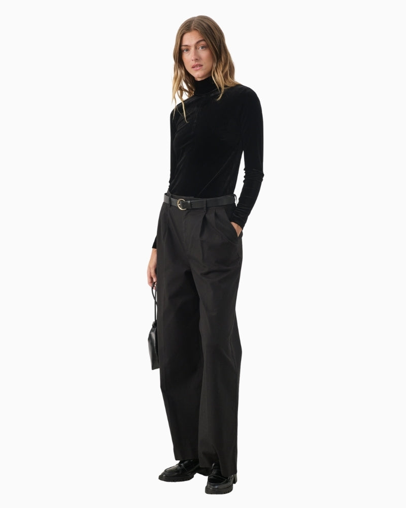 Model wearing black velvet top styled with high-waisted trousers