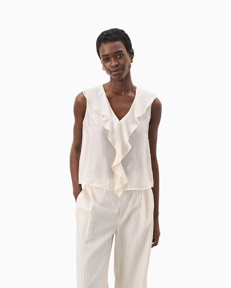 Model wearing ivory sleeveless blouse with front ruffle detail and wide-leg cream trousers