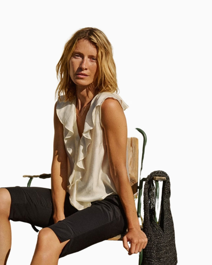 Model styling ivory ruffle blouse with casual shorts for a relaxed yet elegant summer outfit