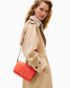 Model view of Tommy flap bag in orange faux leather with gold logo detail